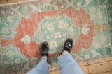 A distressed vintage Oushak rug with terracotta and mint tones, shown to scale in a home.