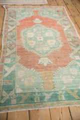 Angled perspective of a distressed Oushak rug showing its faded terracotta and mint green design.