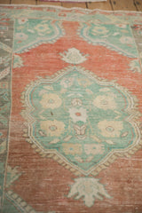 Detail of the worn, low-pile texture on the Oushak rug's mint green and terracotta floral medallion.