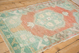 The distressed low-pile texture and mint green corner of a vintage Turkish Oushak rug.