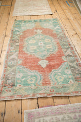 Angled view of a distressed Oushak rug showing its time-softened terracotta and mint green tones.