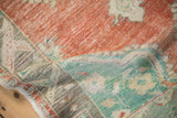 Textural close-up of a folded distressed Oushak rug in soft brick red and pale turquoise green.