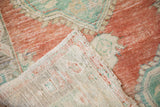 A folded corner on a vintage Oushak rug reveals its hand-knotted foundation and distressed, low-pile texture.