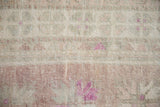 Close-up of the distressed Oushak rug's low, hand-knotted pile in dusty aubergine and ivory.