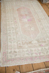 Distressed Oushak rug from an angle, showing mostly even wear across its ivory and aubergine pile.