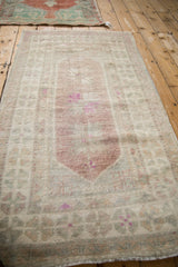 Angled view of a distressed Oushak rug showing its faded aubergine medallion and low-pile texture.