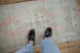 Distressed vintage Oushak rug displaying worn blush and mint patterns on a light ground.