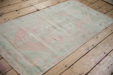 Secured side edge and distressed texture of a vintage Oushak rug in pale blush and mint.