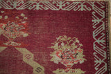 Detail of the antique Anatolian rug's worn pile, silver vine border, and interior floral blossom.