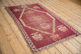 Angled view showing the worn pile and exposed foundation of a red antique Anatolian rug.