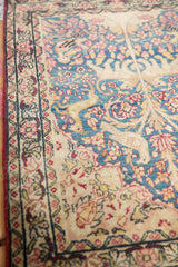 Pictorial antique Kerman rug detail showing blue field with ivory vines and red blossoms.