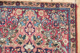 Corner detail of antique Kerman rug, showing sand ground border with floral blossoms, cochineal red field, and intact selvage.