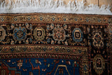 Hand-knotted floral border in navy blue and sand with secured white fringe on a vintage Sarouk rug.