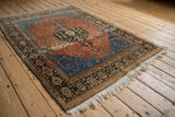 Angled view of a traditional Persian Josan Sarouk rug with a dark medallion and sapphire blue spandrels.