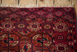 Corner of an antique Turkmen rug showing the geometric snowflake border and ivory fringe.