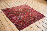 An antique Turkmen square rug angled to show the geometric gul field in burgundy, red, and navy.