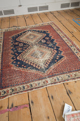 Afshar rug corner showing madder red field, navy serrated contour, germinating plant border, and visible wear.