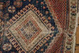 Vintage Afshar rug detail with worn madder red, navy diamond motif and tattered fringe.