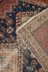Vintage Afshar rug's worn navy and red geometric pile, showing the hand-knotted foundation and tattered fringe.