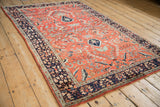 Vintage Sarouk rug from an angle, showing its floral brick-red field and contrasting navy border.