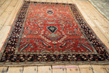 Angled view of a vintage Persian Sarouk rug's vibrant brick-red field and dark navy floral border.