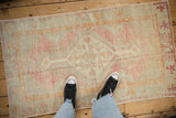 A standing perspective of a vintage distressed Oushak rug showing its faded pink and seafoam green pattern.