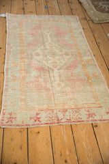 Vintage Oushak rug seen from an angle, highlighting its distressed, faded pink and green design.
