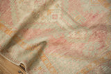 Angled view of the distressed Oushak's low-pile texture in pink, seafoam, and saffron yellow.