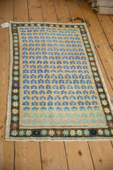 Distressed Oushak rug with faded blue floral blossoms and dark brown starburst border.