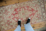Top-down view of the distressed texture and faded raspberry pattern of a vintage Oushak runner.