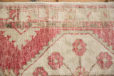 Faded raspberry floral and geometric patterns visible on distressed ivory Oushak rug pile.