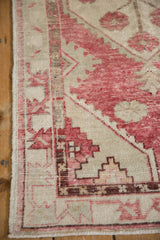 Distressed vintage Oushak rug corner with faded raspberry, ivory, and aubergine geometric patterns.