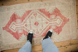 The decorative, distressed texture of a vintage Oushak rug shown underfoot for scale.