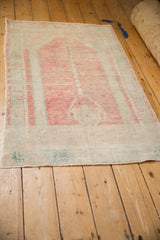 Distressed Oushak rug from an angle, with a pale blush prayer design and faded turquoise details.