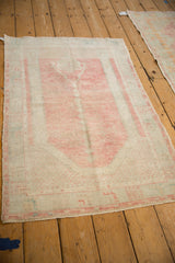 Angled view of a vintage Oushak rug showing its distressed texture and faded blush prayer design.