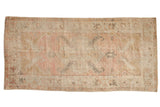 Vintage distressed Oushak rug runner with a time-softened shield medallion in dusty rose, silver, and gold.