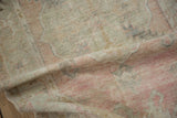 Low, worn pile of a distressed Oushak rug in muted pink and silver tones.
