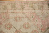 Detailed view of the distressed pile and floral leaf border in dusty rose and olive green.