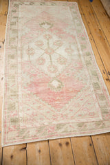 Distressed Oushak rug runner angled to show its faded dusty rose and olive green floral design.