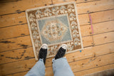 Distressed Oushak rug corner, revealing dusty denim blue, beige, and bronze plant motifs.