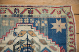 Vintage Oushak rug corner showing dusty blue field, beige starburst, and pale red vine border.