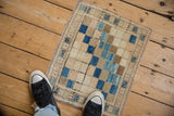 Distressed Oushak rug with diagonal blue, beige squares, plant border, seen with feet for scale.