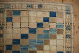 Distressed Oushak rug corner showing diagonal blue, beige squares, and a plant motif border.