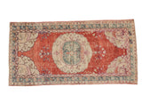 Distressed vintage Oushak runner features a cherry red field, ivory floral medallion, dusty teal, 2'7