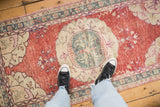 Distressed Oushak runner with worn cherry red field, ivory medallion, and dusty teal patterns.