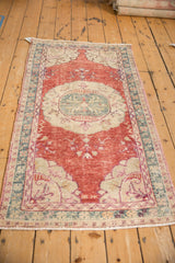 Distressed Oushak rug corner featuring cherry red field, ivory spandrel, and floral teal border.