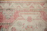 Distressed vintage Oushak rug close-up: worn rose and ivory pile revealing foundation with geometric details.