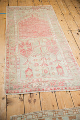 Angled full-length view of a vintage Oushak prayer rug in faded cherry red and sand tones.