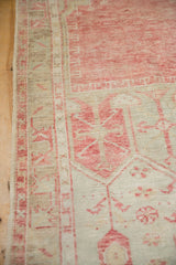 Detail of a vintage Oushak rug's low pile, showing wear and the geometric border in faded red and sand.