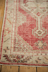 Corner detail of a distressed Oushak rug with low pile showing the red stepped medallion and ivory border.